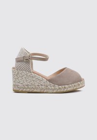 Sandalia de cuña de ante color beige con tira de tejido trenzado en el tobillo, punta cerrada y plataforma de yute trenzado. Superficie texturizada y hebilla ajustable.