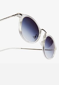 Okrugle sunčane naočale s prozirnim okvirima i gradijentnim ljubičastim lećama. Srebrne metalne drške povezuju leće i imaju suptilni brend sa strane.