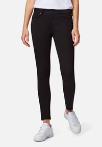 Jeans negros ajustados hechos de denim con una textura suave, que cuentan con una cintura de altura media, bolsillos en la parte delantera y un corte ceñido, combinados con zapatillas blancas.