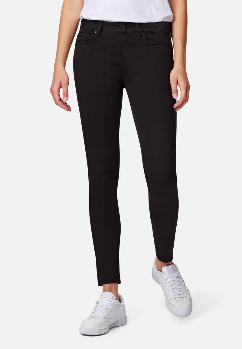 Jeans negros ajustados hechos de denim con una textura suave, que cuentan con una cintura de altura media, bolsillos en la parte delantera y un corte ceñido, combinados con zapatillas blancas.