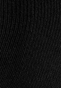 Mustaa neulottua kangasta, jossa on ribbineulosta muistuttava pinta ja aaltoilevia viivoja muodostamassa kuviota. Pinta näyttää pehmeältä ja joustavalta.