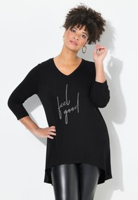Schwarz Tunika mit V-Ausschnitt, drei Viertel Ärmeln und "Feel Good"-Textdesign in silbernen Akzenten. Mit abgerundetem Saum und weichem Stoff.
