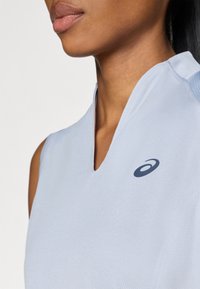 Ανοιχτό μπλε αθλητική μπλούζα χωρίς μανίκια με σχέδιο σε σχήμα V. Διαθέτει λείο υφή και σκούρο μπλε λογότυπο στην αριστερή  περιοχή του στήθους.