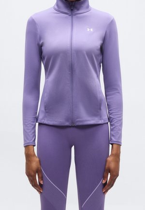 Frau trägt eine eng anliegende lavendelfarbene Jacke mit Reißverschluss und passende Leggings mit dezenten Musterdetails an den Oberschenkeln.