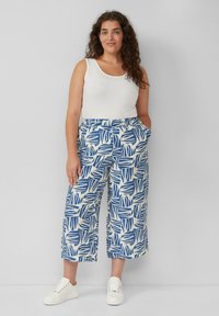 Witte tanktop gecombineerd met blauw-witte culottes met een bladdesign en witte sneakers. Glad materiaal, losse pasvorm.