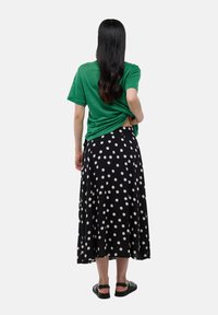 T-shirt vert à manches courtes, jupe maxi à pois noirs et sandales plates noires. La tenue présente une coupe décontractée et un tissu fluide.