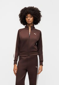 Καφέ αθλητικό τζάκετ με φερμουάρ, με λευκές πλευρικές ρίγες και λογότυπο PUMA· κατασκευασμένο από λείο ύφασμα, διαθέτει όρθιο γιακά και εφαρμοστά μανίκια.