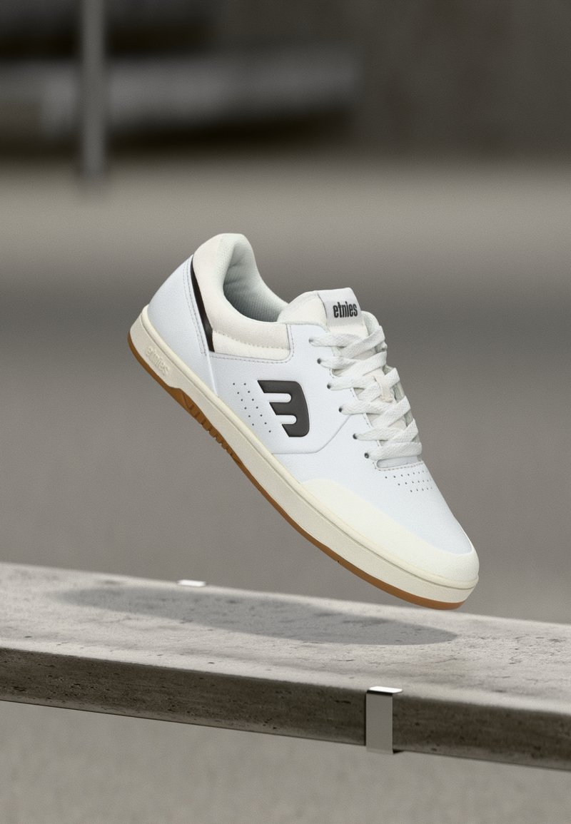 Λευκό δερμάτινο sneaker με μαύρο λογότυπο, διάτρητη περιοχή στα δάχτυλ α και καουτσούκ σόλα. Διαθέτει κορδόνια και επενδεδυμένο κολάρο για άνεση.