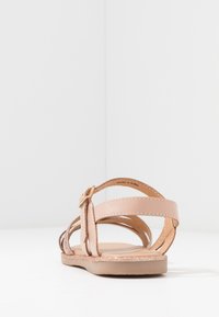 Sandalias de cuero marrón con múltiples tiras y un cierre de hebilla. Presentan una suela plana con un sutil acento de purpurina a lo largo del borde.