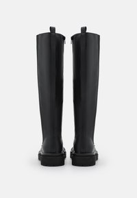 Botas negras hasta la rodilla con un acabado de cuero suave, suelas de goma planas y cremalleras traseras para facilitar el uso.