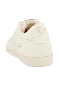 Sneaker color avorio con suola strutturata, scritta "FL" in oro sul tallone e testo "STADION" sul fianco, vista da dietro.