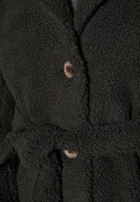 Abrigo de forro polar verde oscuro con una superficie texturizada, que presenta un cierre de botones y un cinturón atado. Tela suave y cálida con costuras visibles.
