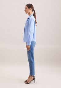 Himmelblaues, gestreiftes Langarmhemd mit Kragen, kombiniert mit geraden Denim-Jeans und schwarzen, römischen Sandalen mit hohen Absätzen.