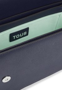 Granatowy portfel ze strukturalnej skóry z miętowym wnętrzem i czarną metką z logo "TOUS". Srebrne okucia z zapięciem na zatrzask.