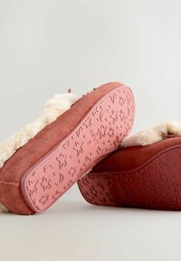 Røde ruskinds slip-on tøfler med en foring i kunstpels. Sålen har et tekstureret design med stjerner og måner, der giver godt greb.
