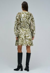 Vestido de manga larga, con un patrón en verde y blanco, con cintura ceñida, combinado con botas negras de tacón alto. Tejido suave con un diseño fluido.