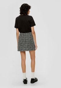 Zwarte top met korte mouwen gecombineerd met een minirok van grijs tweed met textuur, voorzien van een ritssluiting aan de achterkant. Model draagt zwarte schoenen en witte enkelsokken.