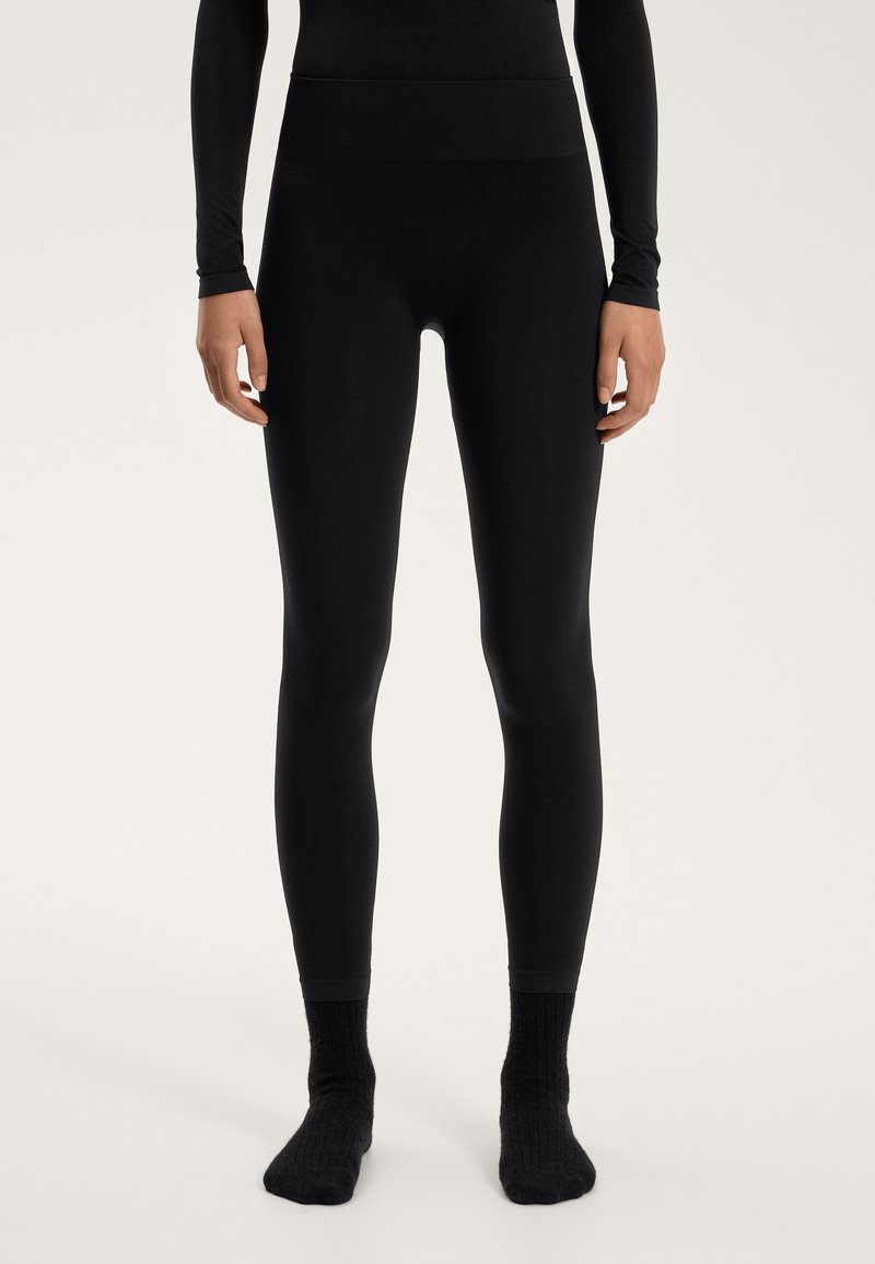 Zwarte leggings van glad, rekbaar materiaal met een hoge tailleband. Geen zichtbare naden of patronen; aansluitende pasvorm tot aan de enkels.