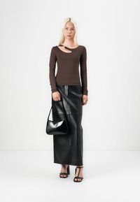 Maglietta marrone a maniche lunghe con dettaglio a taglio, abbinata a una gonna maxi in pelle nera, tacchi neri con lacci e una piccola borsa nera.