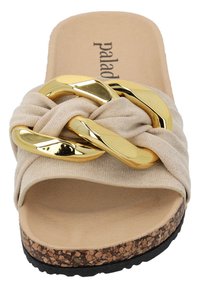 Sandale à glissière beige avec un dessus en tissu texturé doux, présentant un design tordu et un accent en chaîne métallique dorée. Semelle en liège avec une base noire.