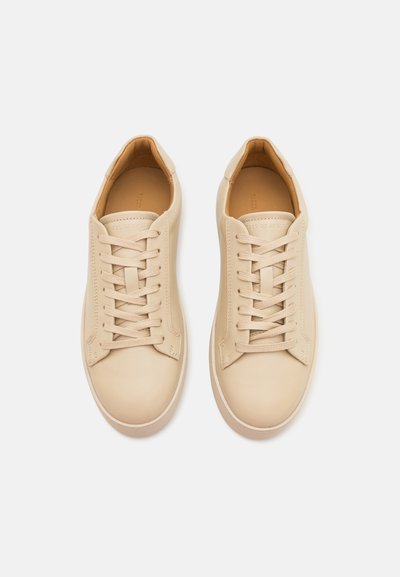 Beige leather sneakers with round toe, flat laces, minimal stitching, and a soft texture. Interior lined in a light tan color.