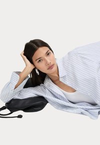 Camisa de botones de rayas azul claro y blanca con mangas largas, corte relajado, llevada sobre una camiseta blanca, combinada con un bolso negro.