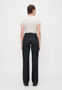 Black high-waisted jeans with a straight leg, five pockets, and a clean design. Paired with a light beige fitted t-shirt. Smooth fabric.