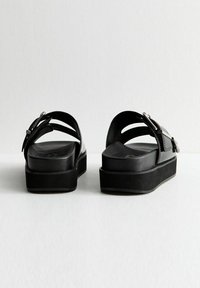 Černé platformové sandály s křížovými popruhy a stříbrnou sponou, mají hladký povrch a zaoblenou špičku.