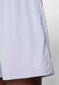Světlé fialové sportovní šortky z texturované látky, s malým bílým logem Nike na dolním lemu a bočními rozparky pro volnost pohybu.