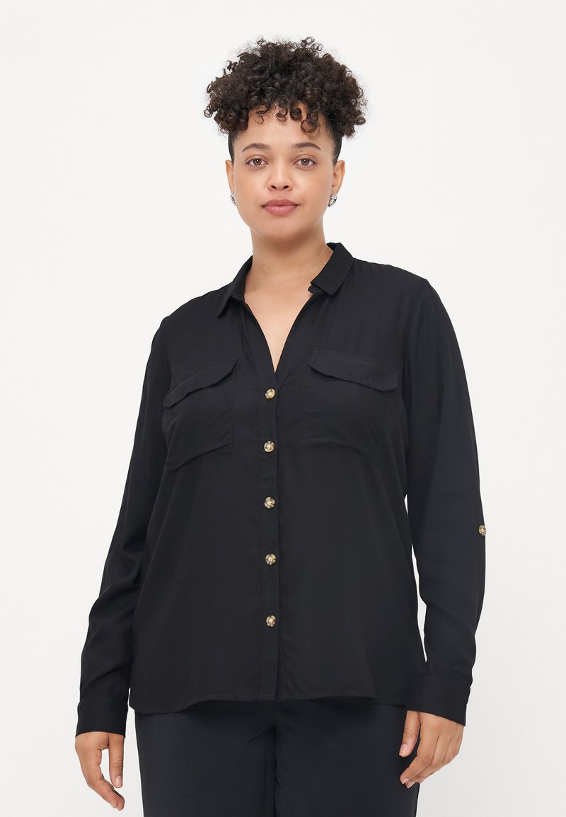 Chemise noire à manches longues en tissu léger avec un devant boutonné, deux poches poitrine et des boutons dorés. Texture lisse, coupe décontractée.