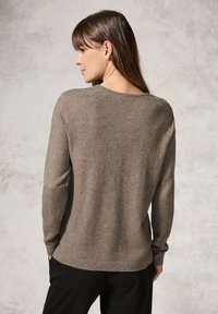 Ruskea neulepaita, jossa on pyöreä pääntie, pitkät hihat ja ribbireunat. Kangas näyttää pehmeältä ja siinä on hienovarainen rakenne neutraalilla taustalla.