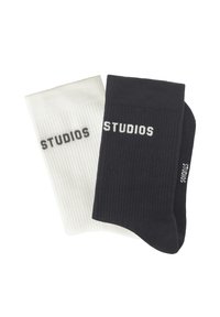 Gerippte Crew-Socken in Schwarz und Weiß. Jede trägt das Wort "STUDIOS" in kontrastierender Strickoptik. Funktionales Design mit strukturierter Oberfläche.