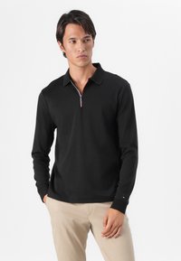 Zwarte langemouwen polo shirt met een rits halsopening en rode accenten. De stof lijkt soepel, met een aansluitende silhouet en contrasterende mouwen.