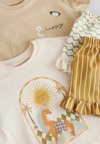 To grafiske t-shirts: beige med broderet bi og blomster, cremefarvet med en enhjørning; plus to mønstrede shorts i grøn og striber.