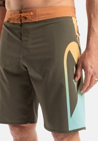 Herrarnas badshorts i olivgrön med ett brunt midjeband. Har en blå-grön gradient och ett framträdande svart logomönster på sidan.