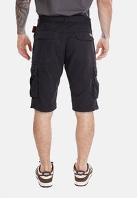 Pantaloni cargo neri in cotone con multiple tasche laterali. Presentano una vita con cintura e dettagli cuciti. Indossati con scarpe casual.