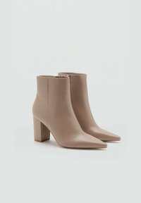 Bottines beiges en cuir lisse avec un bout pointu, un talon bloc et une fermeture éclair sur le côté. Design minimaliste et finition élégante.