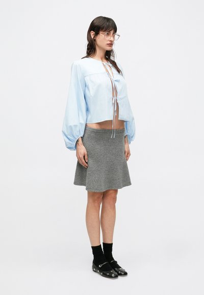 Γαλάζιο κοντό μπλουζάκι με μπαλούν μανίκια και δέσιμο μπροστά, συνδυασμένο με γκρι πλεκτή φούστα σε γραμμή Α. Παπούτσια: μαύρα, φλατ, με τρουκς.