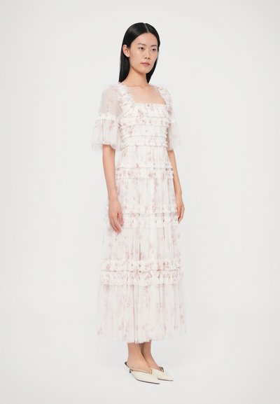 Długa, warstwowa sukienka z przejrzystej, różowej tkaniny w kwiaty. Ma falbaniaste rękawy, kwadratowy dekolt i zwiewny krój.