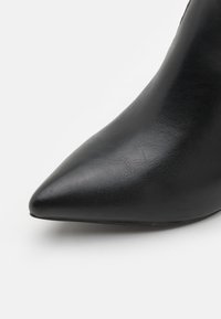 Black leather pointed-toe high heel shoe with a textured surface, a sleek design, and a slender heel, viewed from the side.