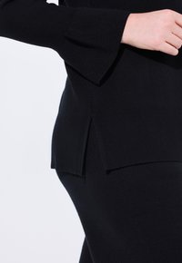 Czarny sweter dzianinowy z bufiastymi rękawami, bocznym rozcięciem i prążkowanymi detalami u dołu. Miękka faktura z jednolitą konstrukcją.