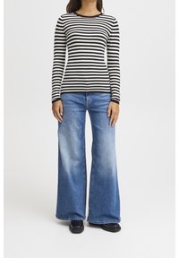 Svart- och vitrandig långärmad topp kombinerad med ljusblå utsvängda jeans. Outfiten har en figurnära passform och svarta platta skor.