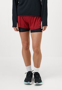 Punased ja mustad spordilühikesed püksid sobiva sisemiselt voodriga, kerge kangaga ja kontrastse vöökohtadega, millele on lisatud mustad jooksukingad.
