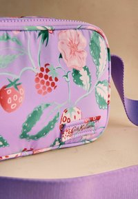 Sac bandoulière lavande avec motif fraises, framboise, fleur rose, feuilles vertes, et bandoulière lavande assortie sur surface beige.