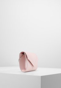 Różowa torebka o gładkim, zaokrąglonym kształcie. Wykonana z teksturowanego materiału, z klapką na zakładkę i srebrnym łańcuszkowym paskiem.