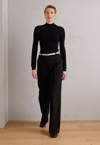 Maglietta nera a maniche lunghe abbinata a pantaloni neri a vita alta e gamba larga, accentuata da una cintura bianca. Texture lisce, design minimalista.