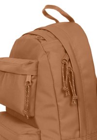 Sac à dos en tissu marron avec une finition texturée, plusieurs poches, des fermetures à cordon réglables et une poignée supérieure solide.