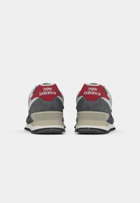 New Balance sneakers med en grå ruskindsøvre, røde accenter på hælen og logoet, en hvid mellemsål og en sort gummisål.