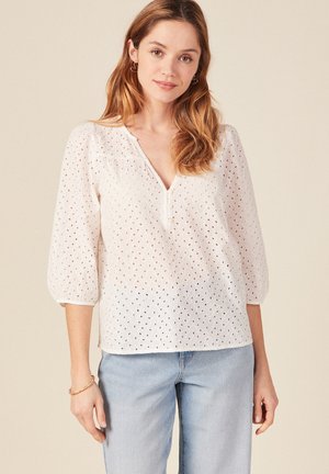 Witte blouse van oogjesstof met V-hals, knopen op de borst en ballonmouwen. Losse fit en textuurpatroon detail.