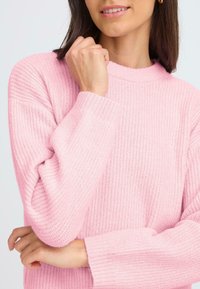 Pulover tricotat de culoare roz pal, cu textură căptușită, guler rotund și mâneci lungi. Designul are o croială lejeră și detalii texturate.